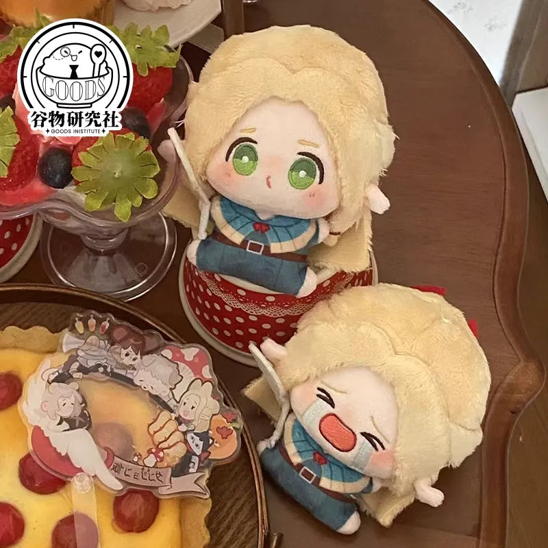 Two adorable mini plush keychains of Marcille from Delicious in Dungeon (Dungeon Meshi) posed in front of a giant, mouthwatering pizza. One keychain shows Marcille with a round, pouty 'bun face' and flushed cheeks, while the other depicts her crying dramatically with teardrops. Both feature her signature blonde hair, pointy elf ears, and soft squishy fabric. The golden cheese and colorful toppings of the pizza make it look irresistibly delicious, creating a fun contrast with Marcille's exaggerated expressio