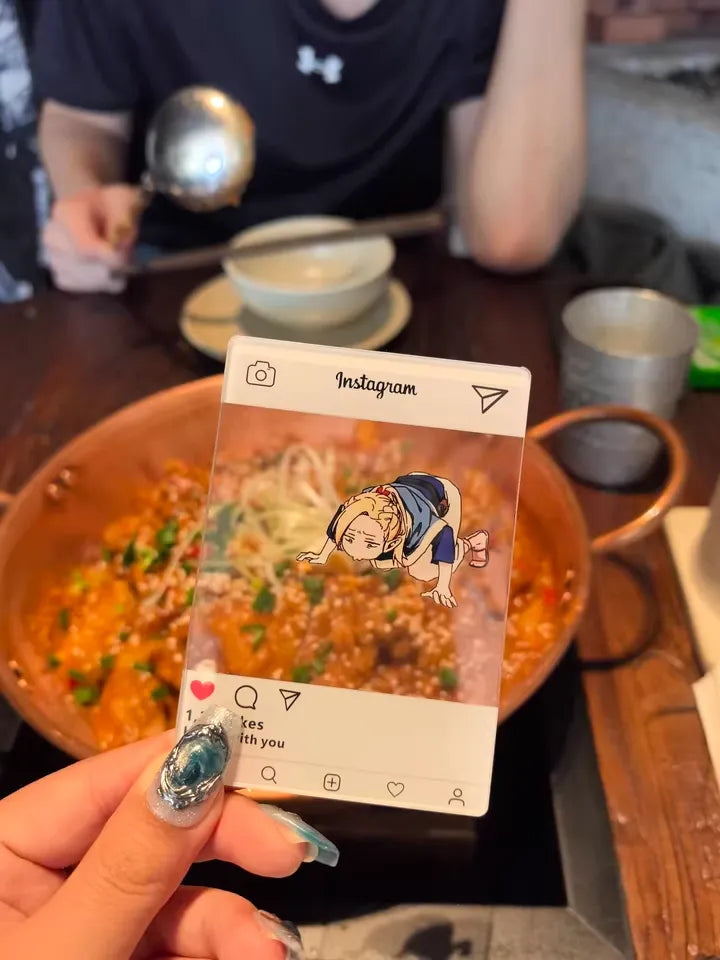 An acrylic transparent card featuring Delicious in Dungeon (Dungeon Meshi)'s Marcille in a comical pose—lying flat on the ground, desperately inhaling the scent of food with starry-eyed obsession. The card is playfully placed next to an aromatic dish (e.g., a sizzling steak or buttery pastry), creating the illusion that Marcille is literally fangirling over the meal. The translucent acrylic blends the artwork with the real food, enhancing the humor of her dramatic antics.